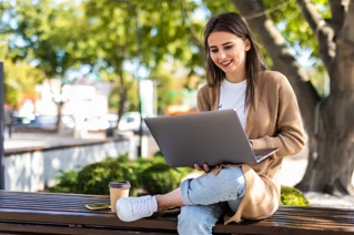 En tjej som jobbar utomhus i en park, med en laptop i knät.